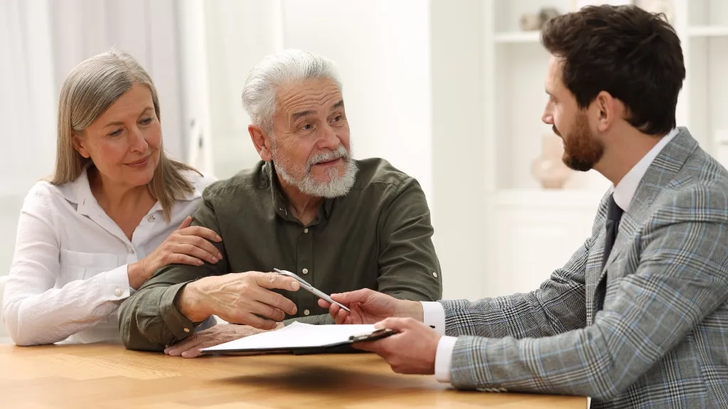 Elderly couple consulting professional man in gray plaid suit at wooden table.
