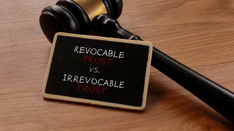 Wooden judge's gavel resting on a table next to a blackboard with text "Revocable Trust vs. Irrevocable Trust.