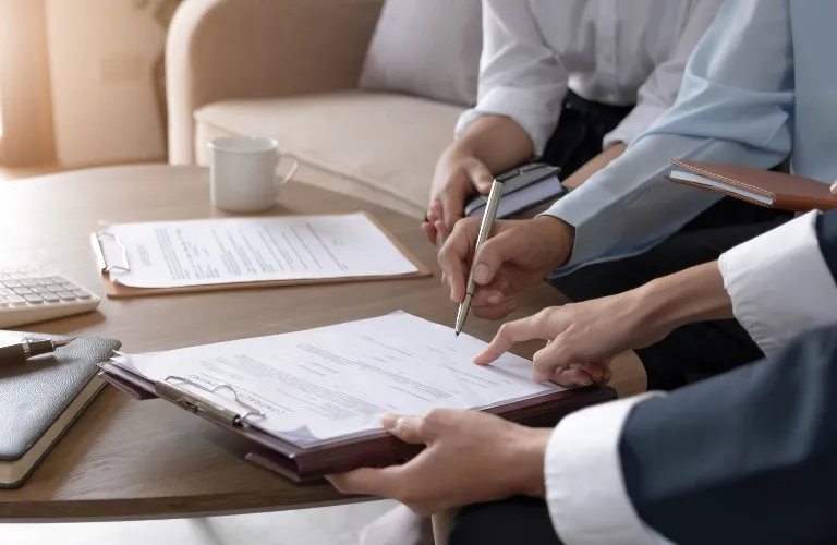 Two professionals reviewing and signing documents on a wooden table in an office setting.