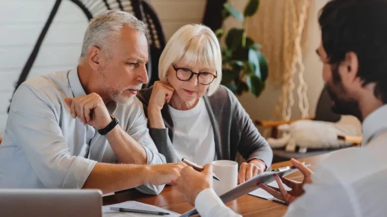 Elderly couple attentively reviewing documents with a professional in a cozy office setting.