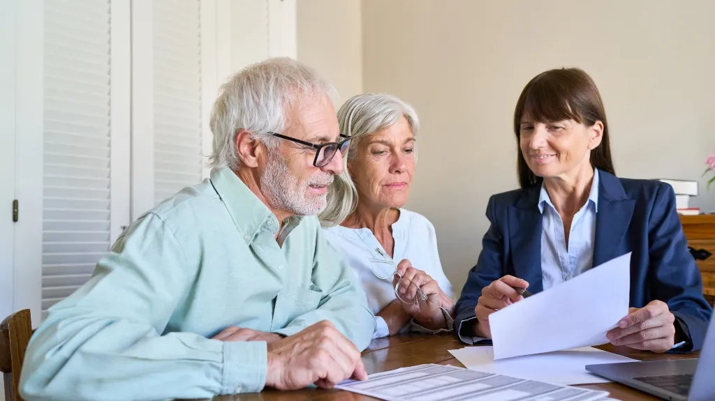 Three adults, two seniors and a professional woman, reviewing documents at a wooden table.
