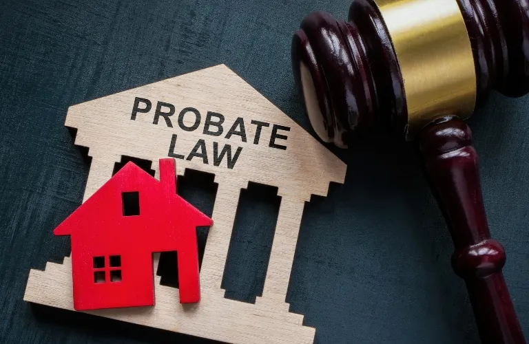 Wooden courthouse model labeled "Probate Law," red house cutout, and judge's gavel on dark surface.